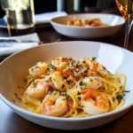 Plate of shrimp scampi with pasta garnished with parsley and lemon slices.